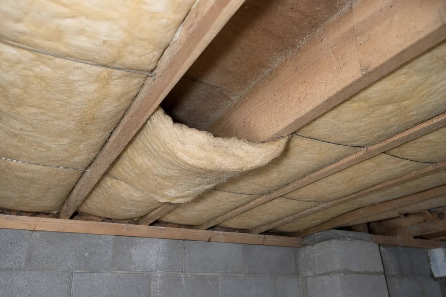 Fiberglass batt insulation sagging out of one floor joist bay where its support wire has slipped